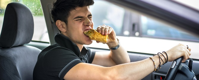 Young man driving his car while eating food